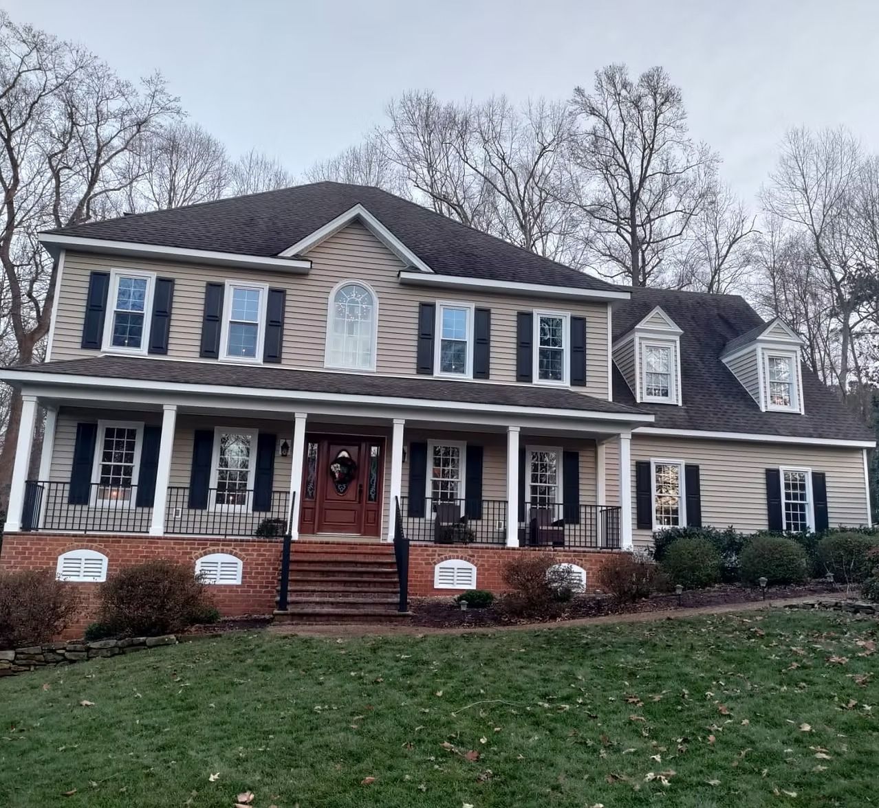 Two-story suburban house with brick porch, white siding, dark shutters, and leafless trees in front yard