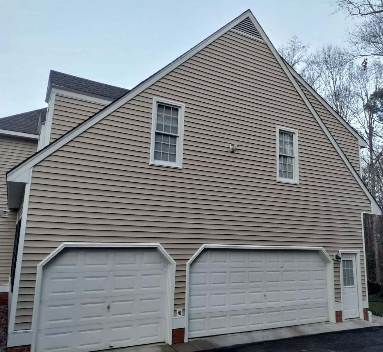 Side view of a beige house with two white garage doors and a steep roof.