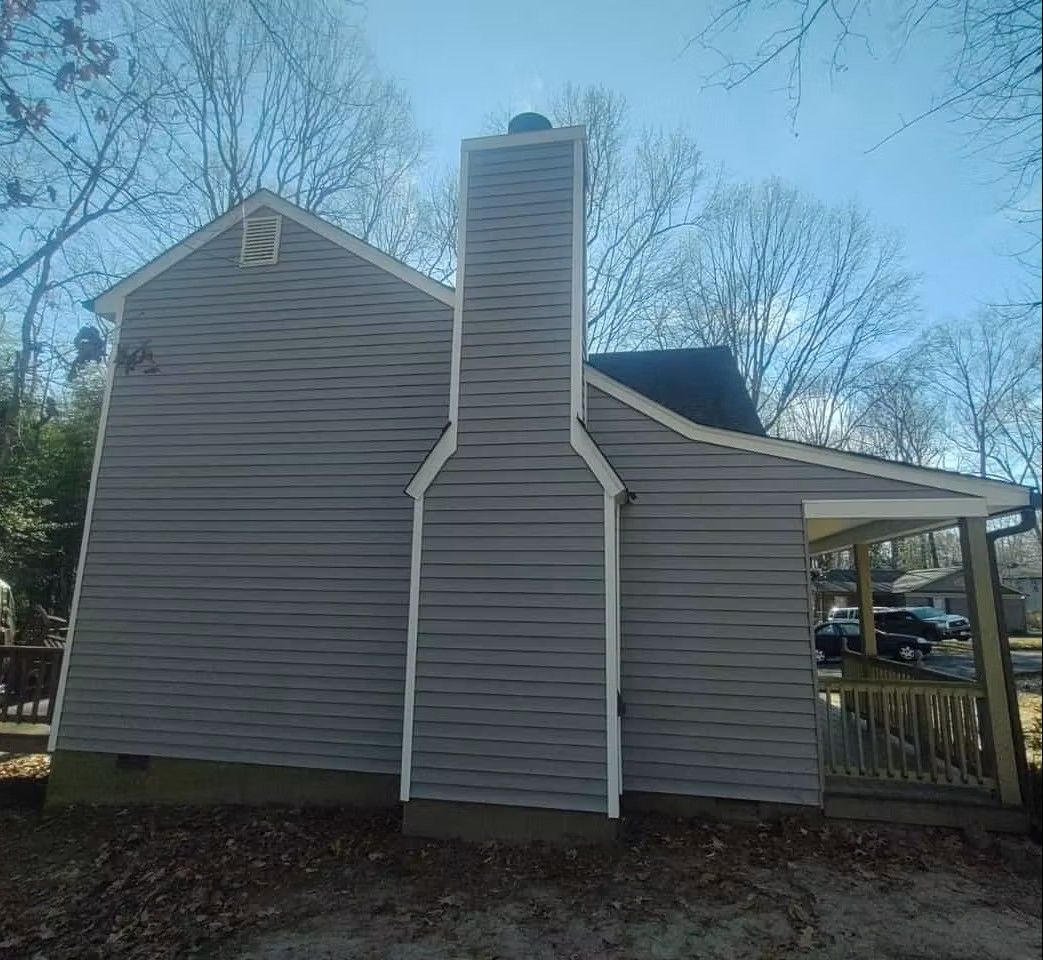 Back view of a gray house with a central brick chimney and a small covered porch on the right