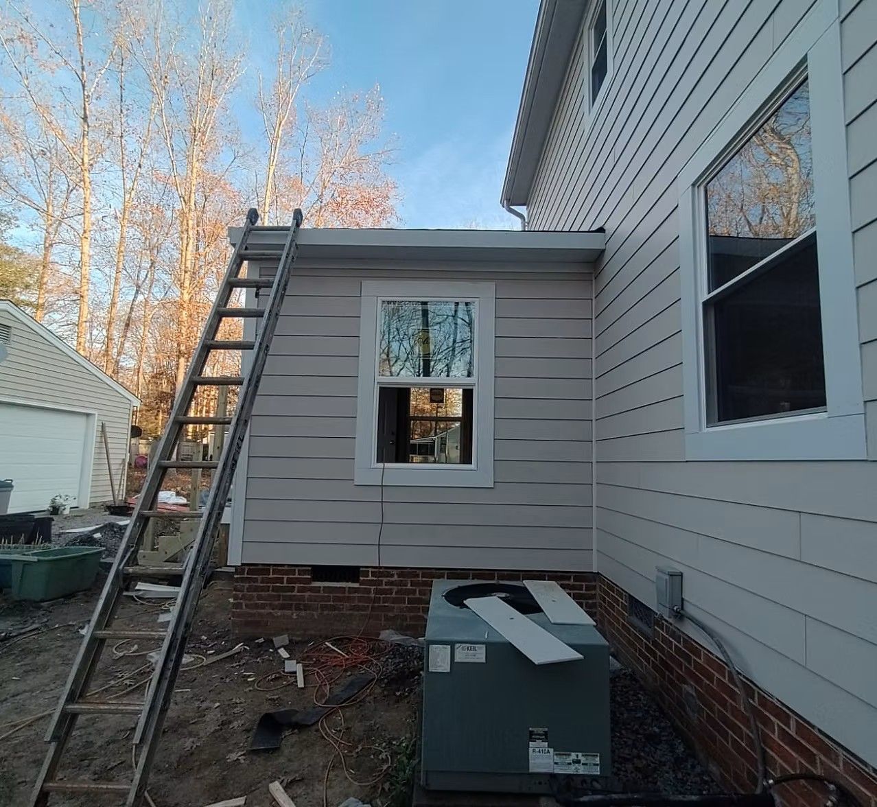 House exterior with a ladder leaning beside a small window extension and an air conditioning unit below.