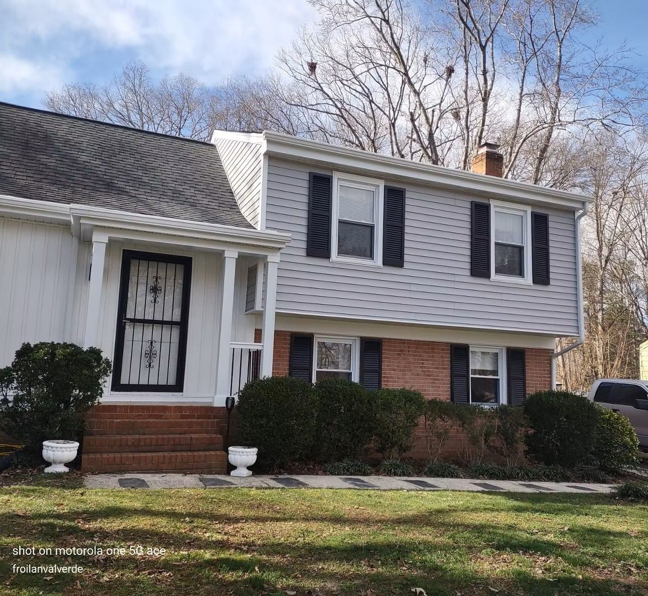 Suburban split-level house with white siding, black shutters, brick accents, and a front lawn