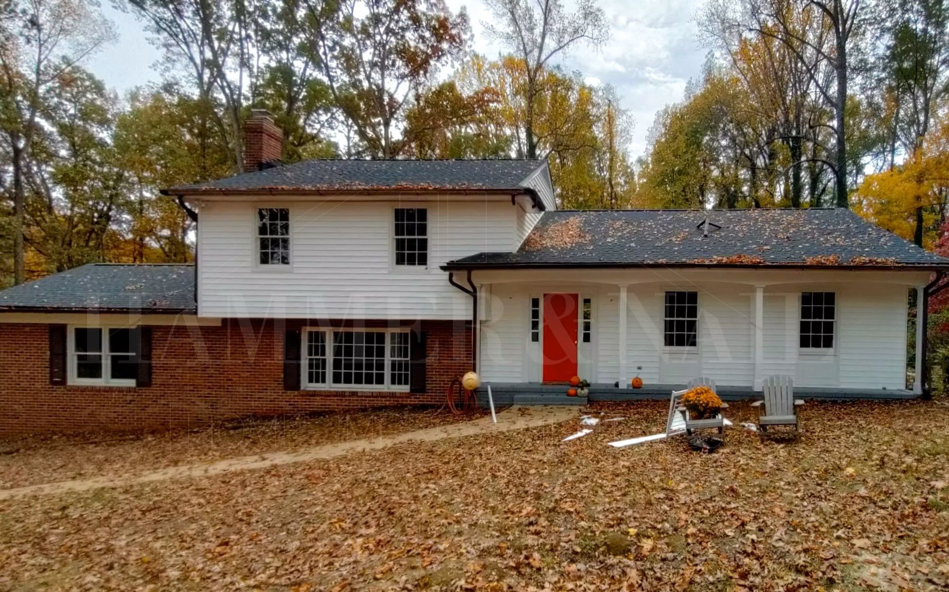 Two-story house with red front door, brick and white siding, surrounded by fallen autumn leaves.