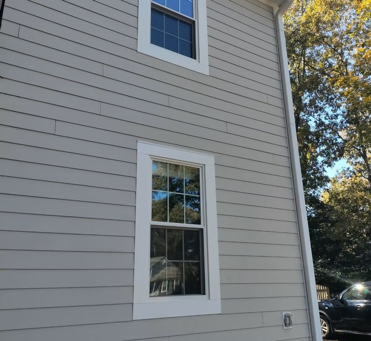Gray house exterior with two white-trimmed windows and trees in the background