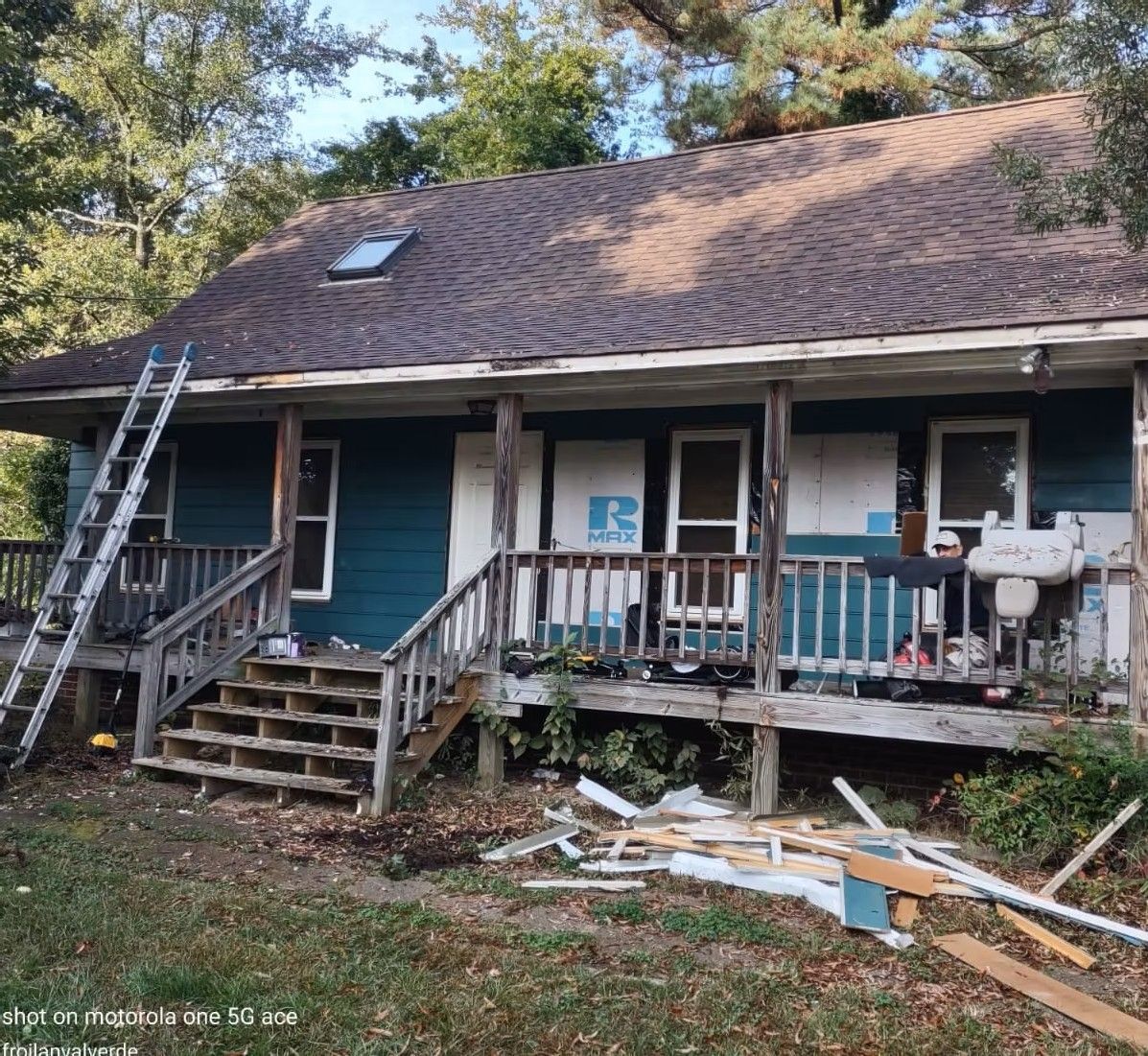 Damaged house exterior with fallen porch debris, ladders, and scattered boards after storm damage