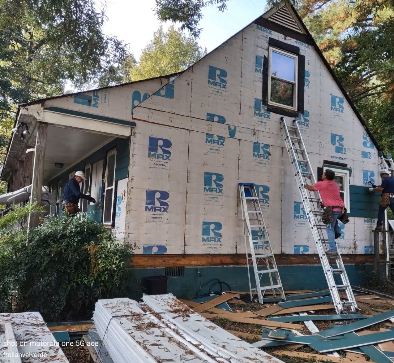 Workers install siding on a house under renovation, with ladders and construction materials outside.