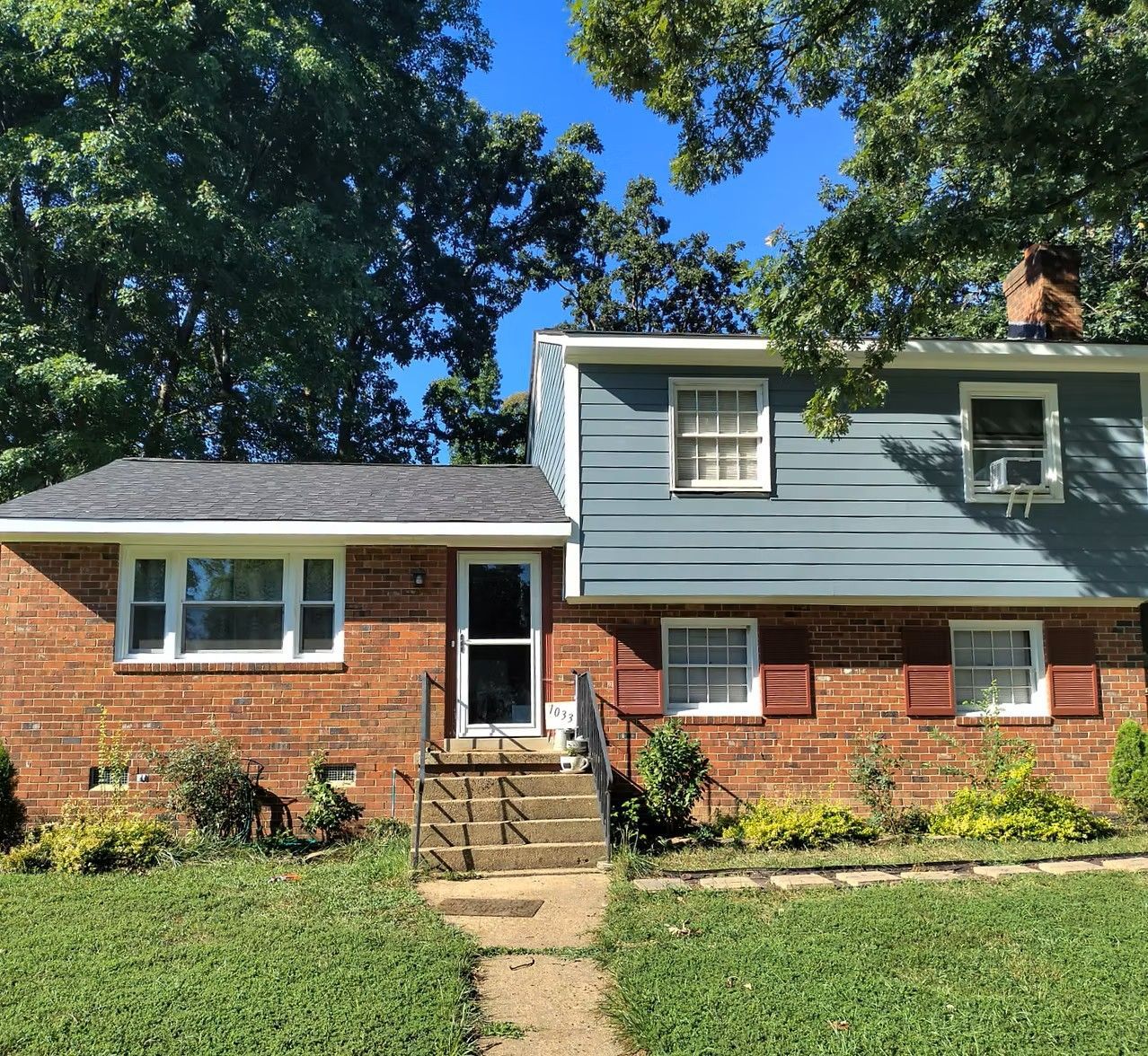 Brick and blue-gray suburban house with front steps and green lawn under trees