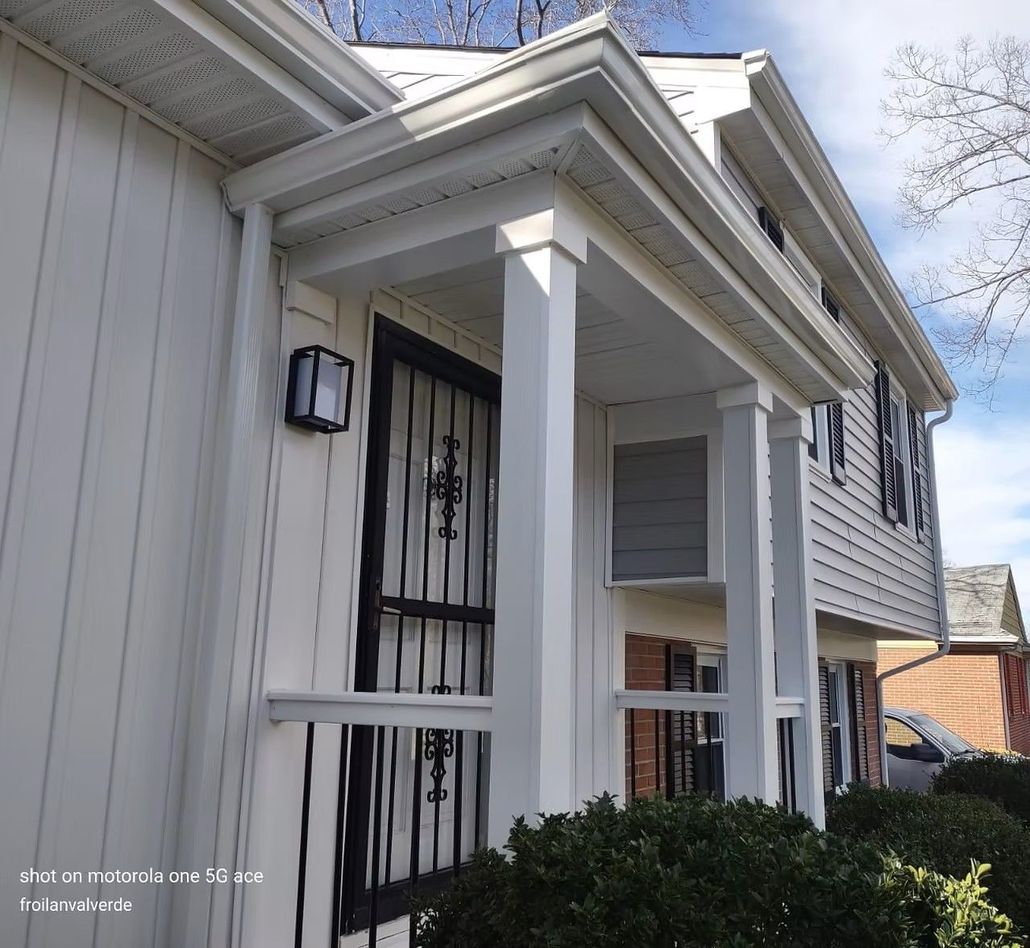 Front porch of a white house with decorative columns, black security door, and shrubbery.