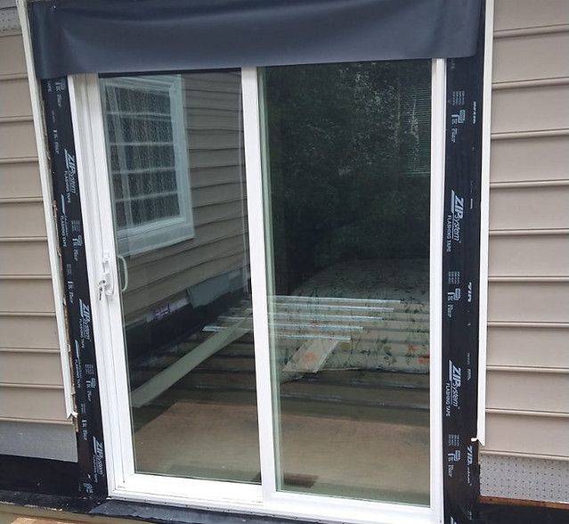 Sliding glass door being installed in a house exterior with black trim and white siding.