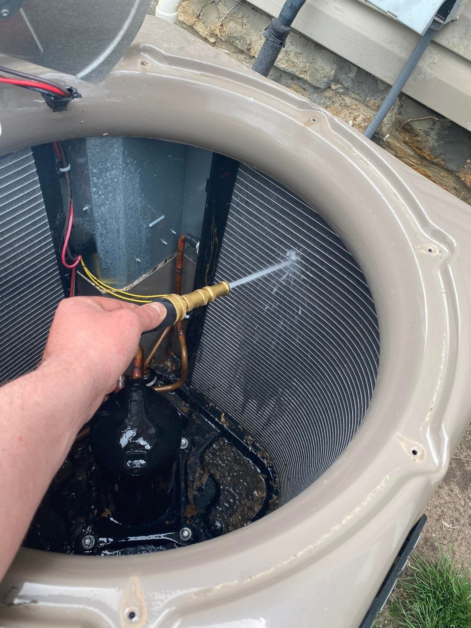 Person spraying water inside an air conditioner unit with a hose, outdoors.