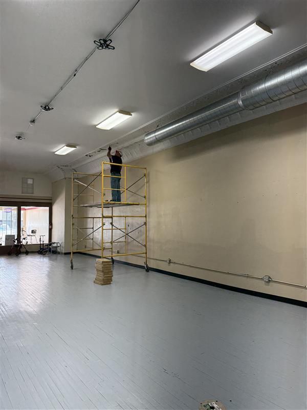 Person on scaffolding working on ceiling electrical in a bright, empty room with gray flooring