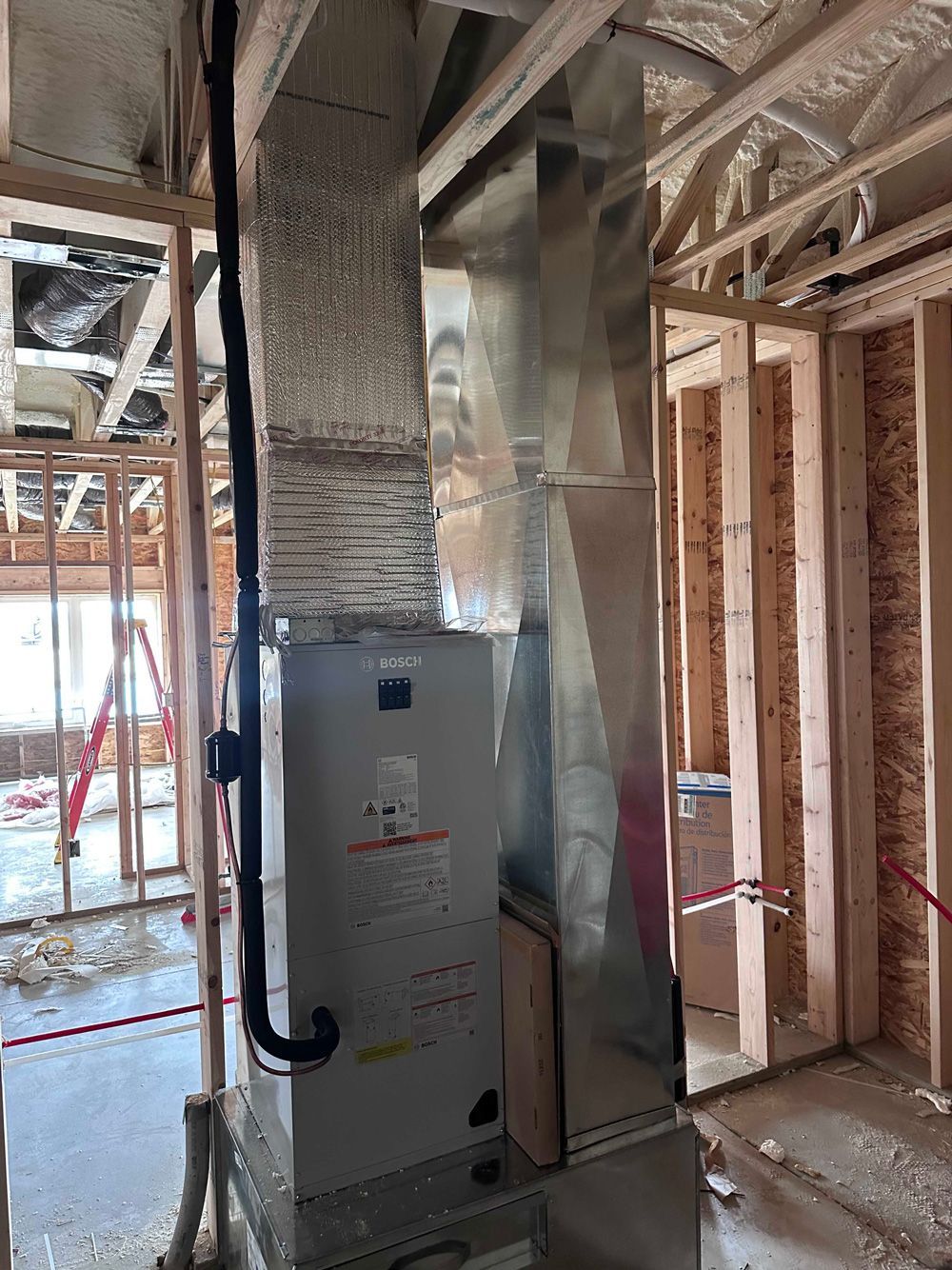 Furnace and ductwork installed in a house under construction, wooden frame visible.