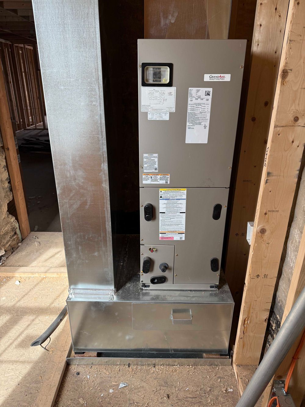 HVAC unit in unfinished room, with ductwork. Beige unit, silver ducts and base.
