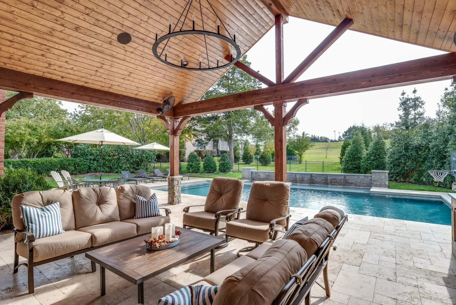 a patio with a couch , chairs , table and umbrellas next to a pool