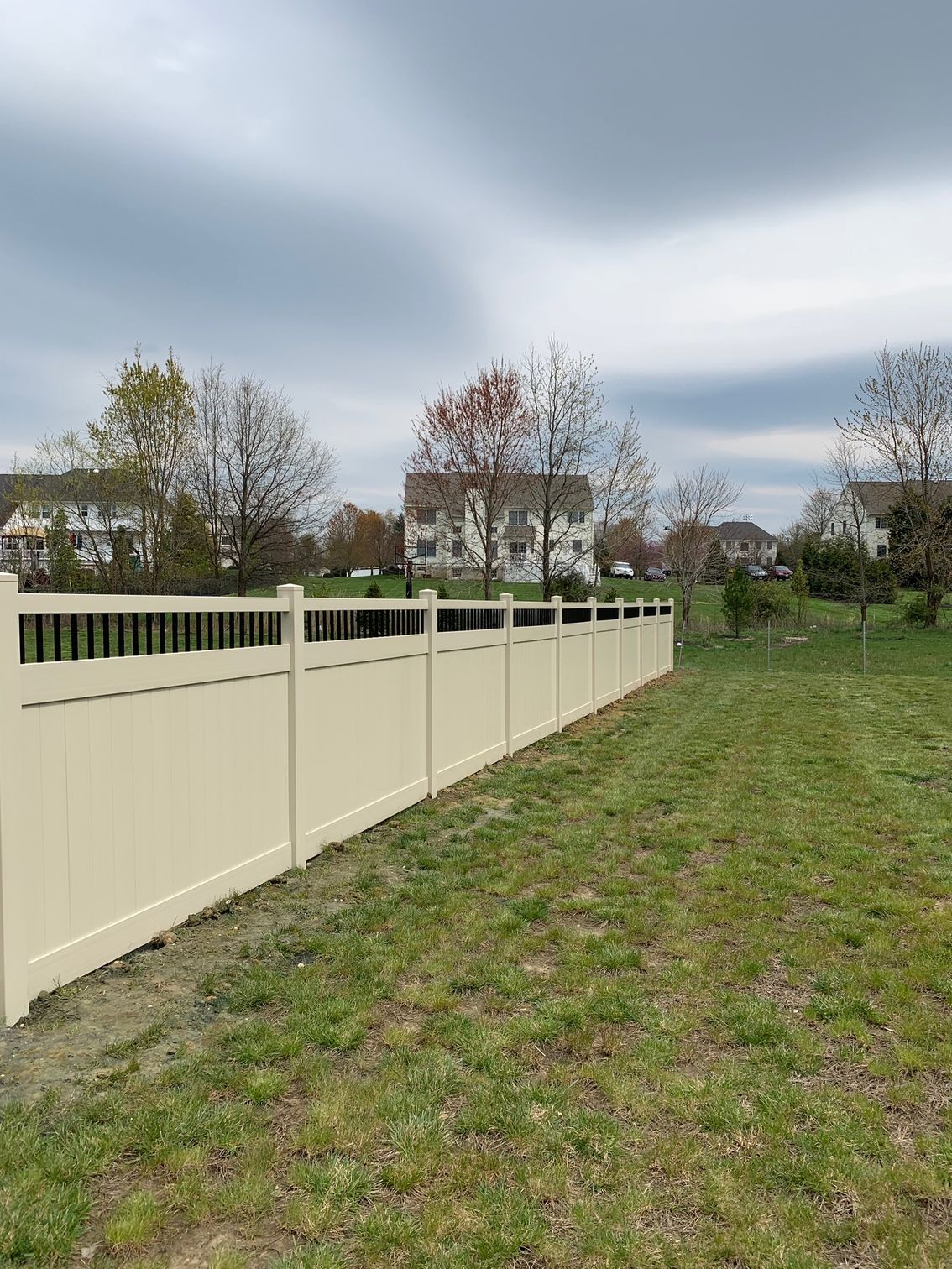 A white fence surrounds a grassy field with a house in the background.