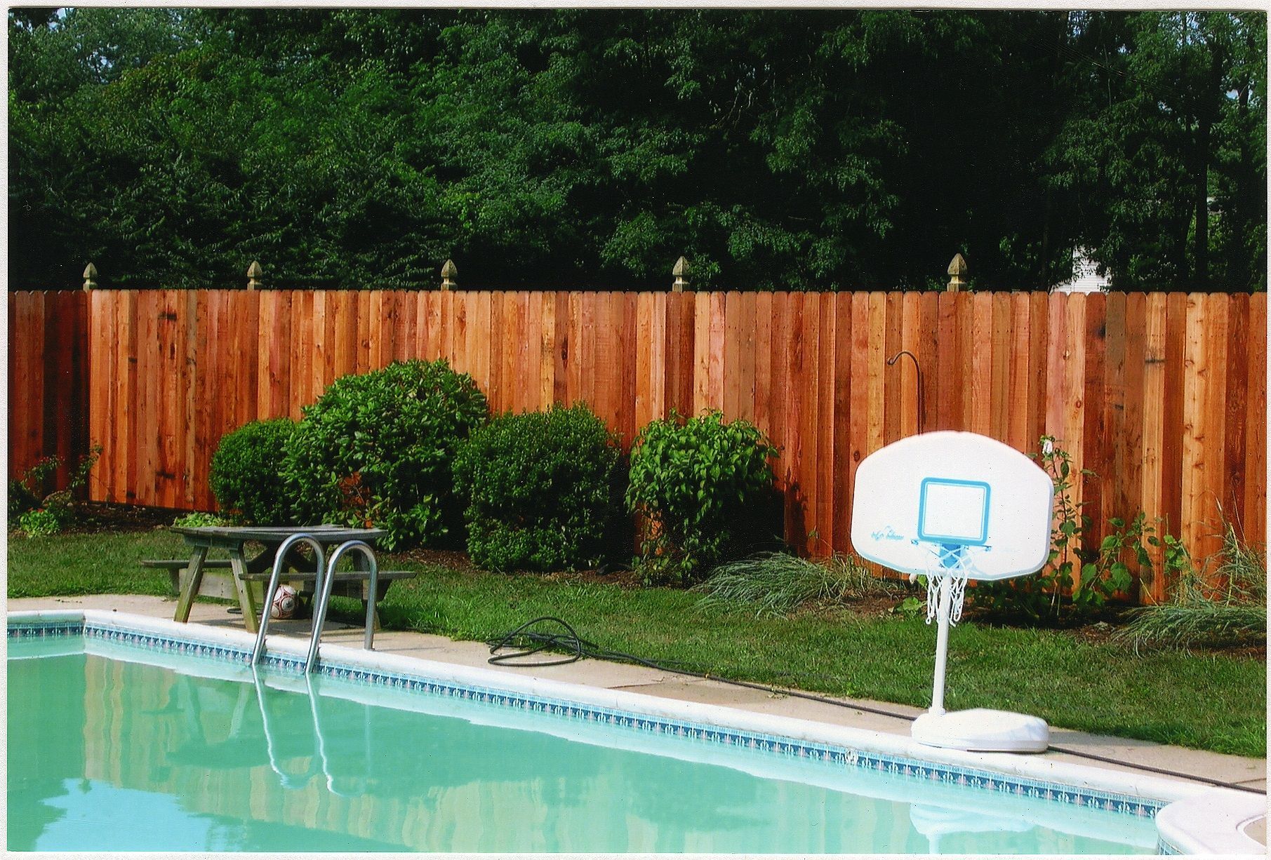 A pool with a wooden fence and a basketball hoop