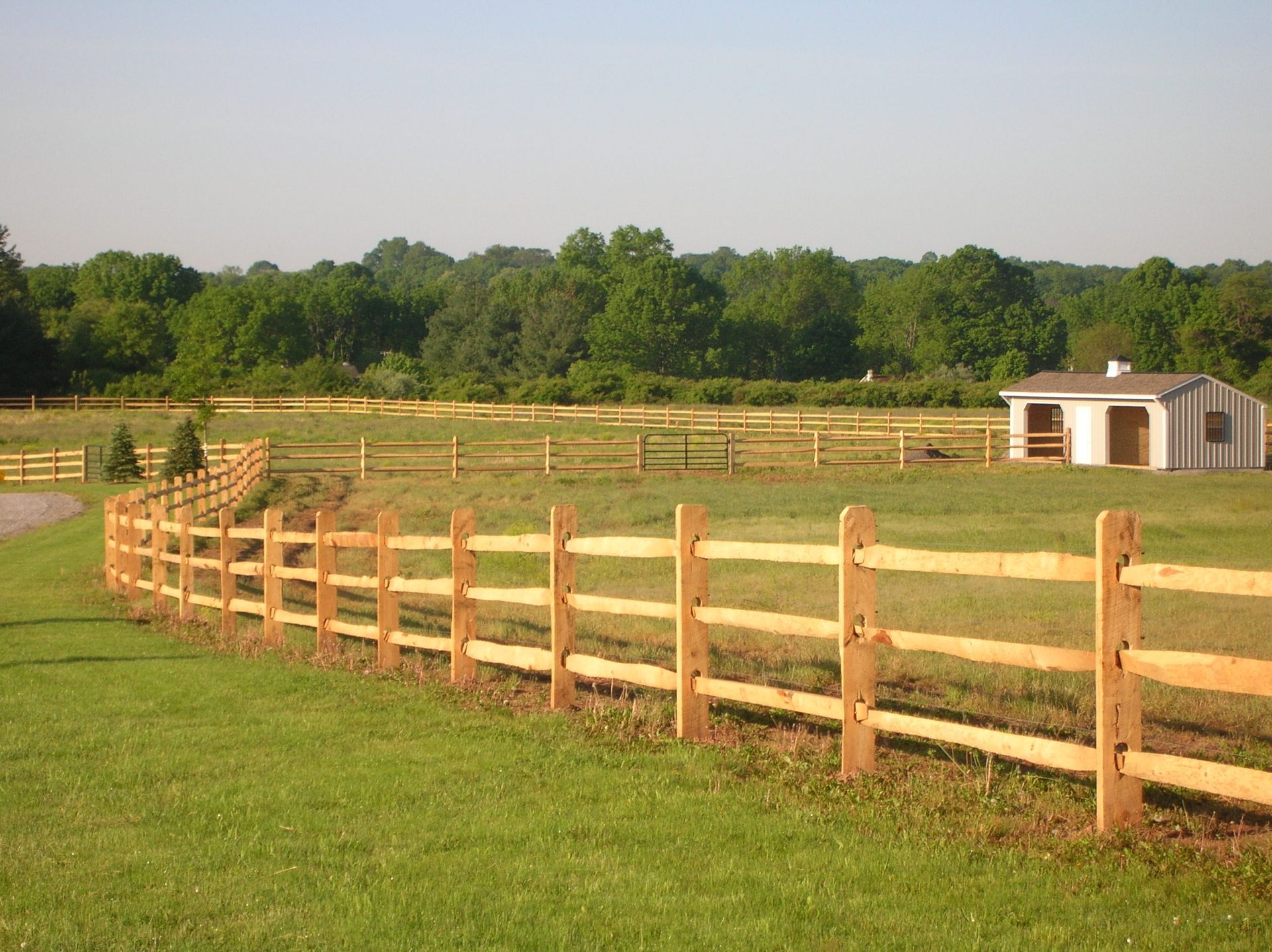A wooden fence surrounds a lush green field with a house in the background.
