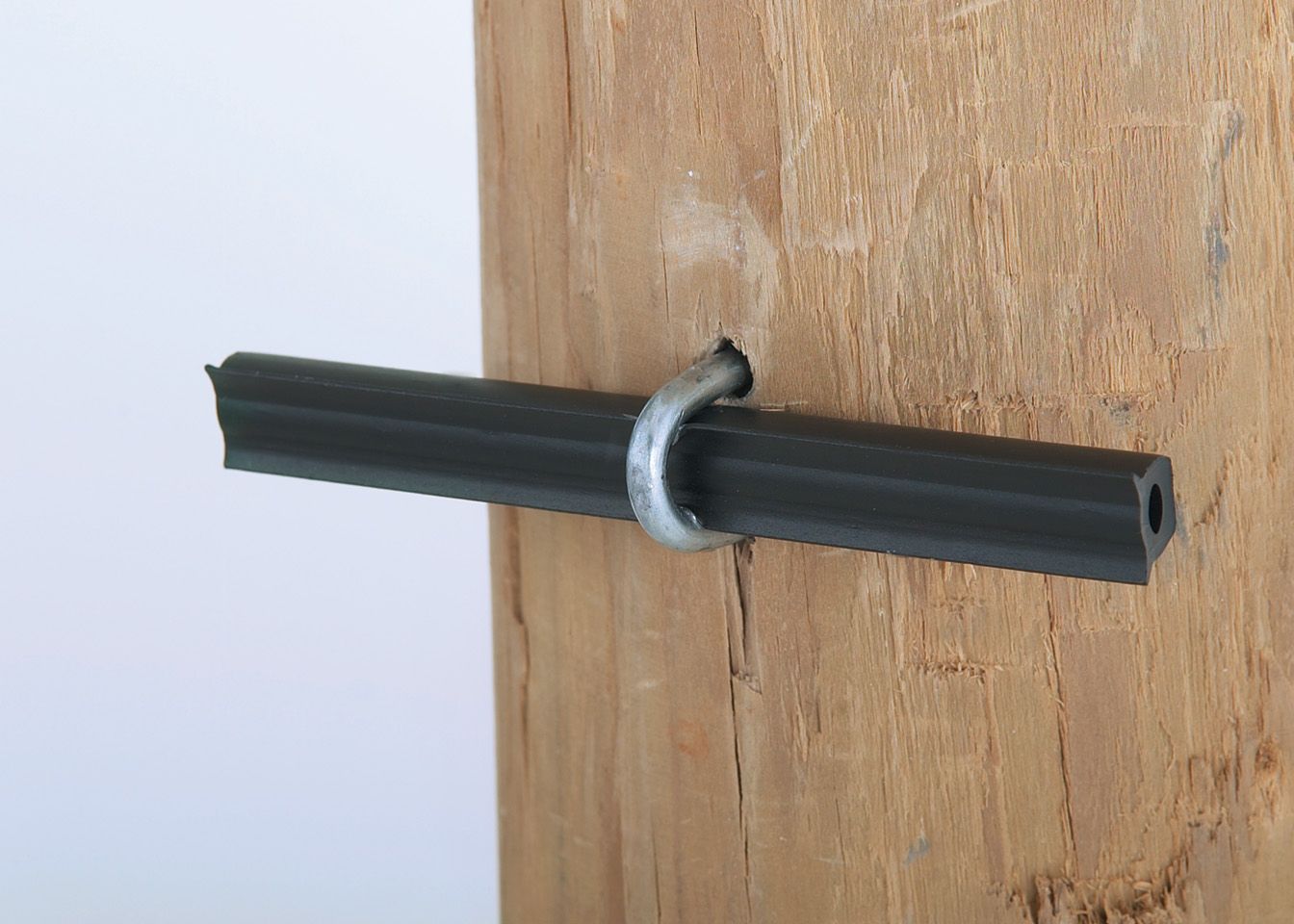 A black pipe is attached to a wooden post with a metal ring.