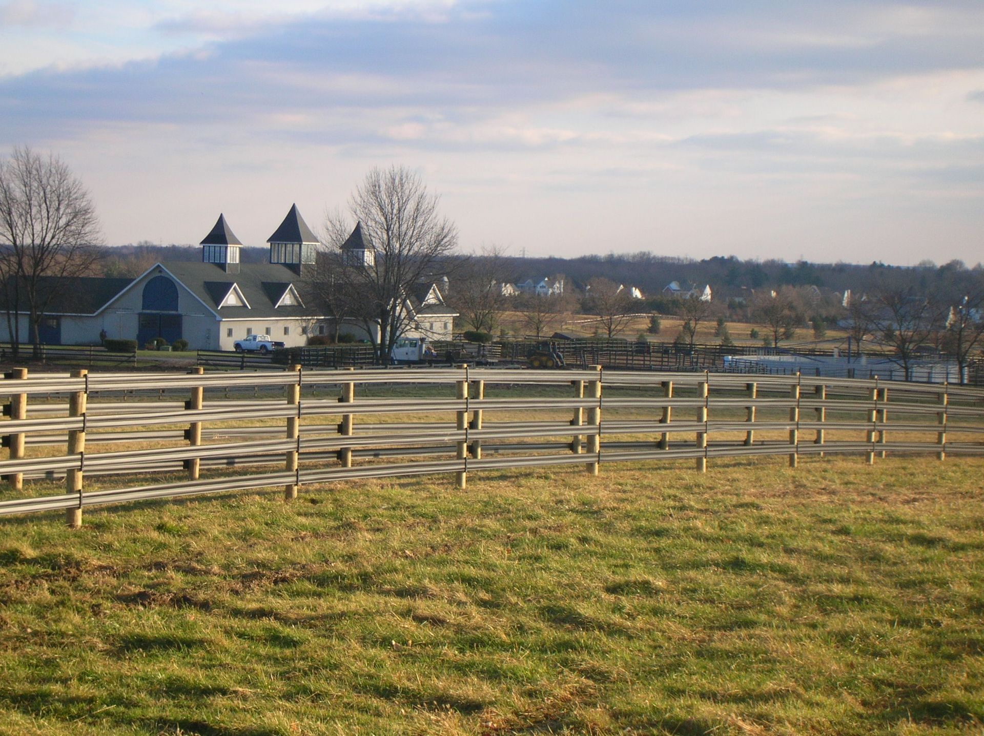 A wooden fence surrounds a grassy field with a white building in the background