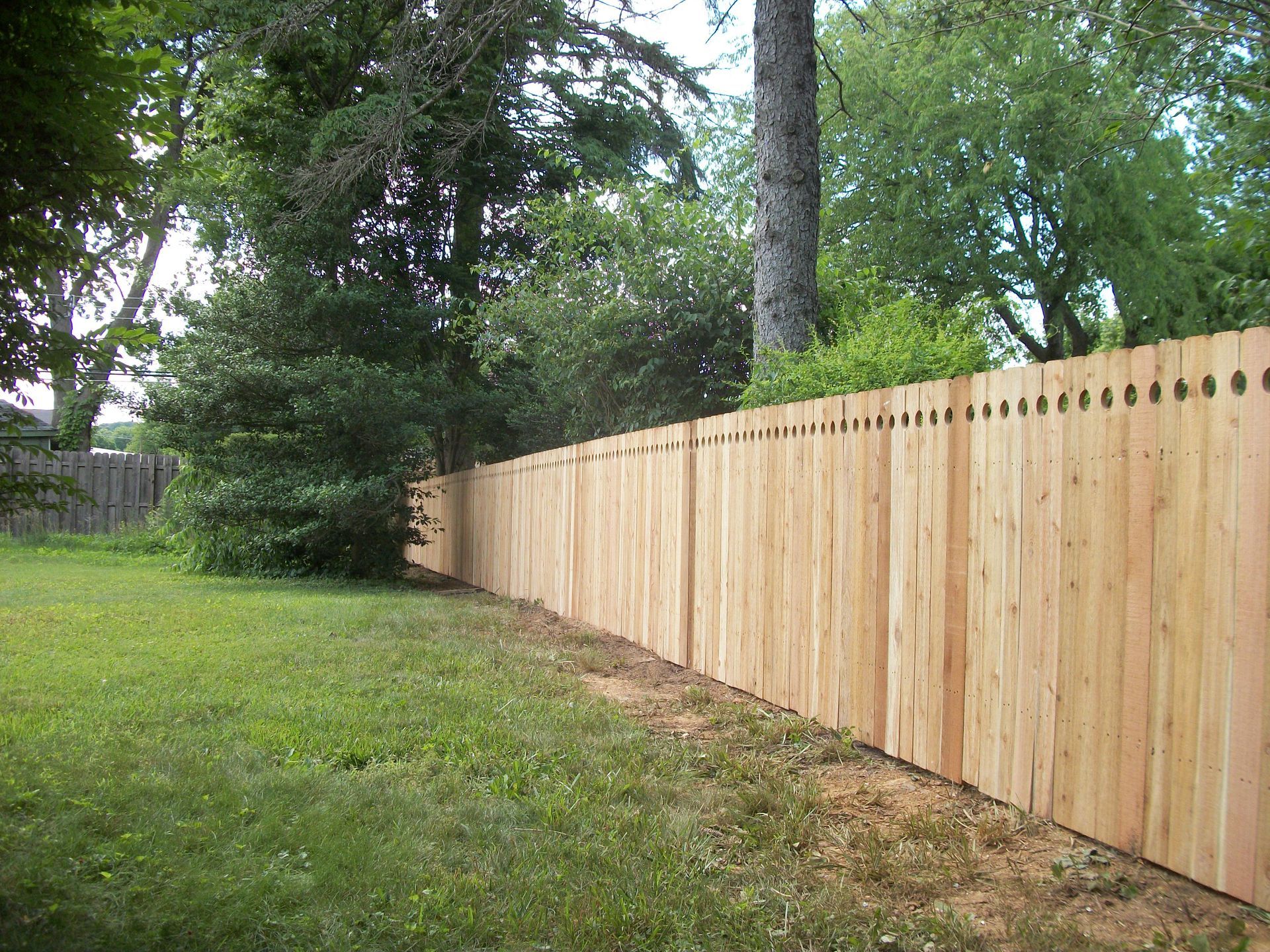 A long wooden fence surrounds a lush green yard.