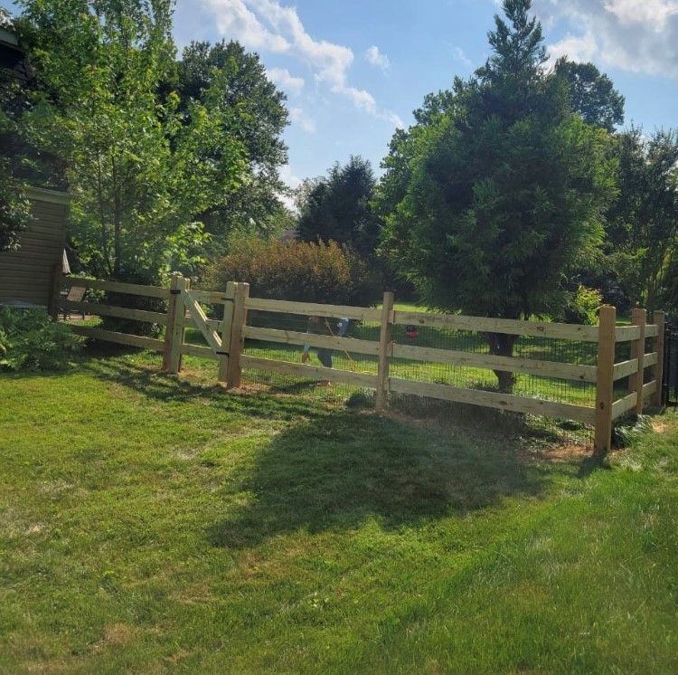 A wooden fence is in the middle of a lush green field.