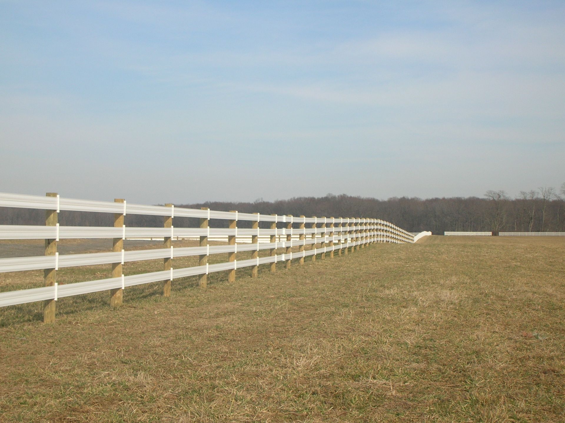 A white fence surrounds a grassy field on a sunny day