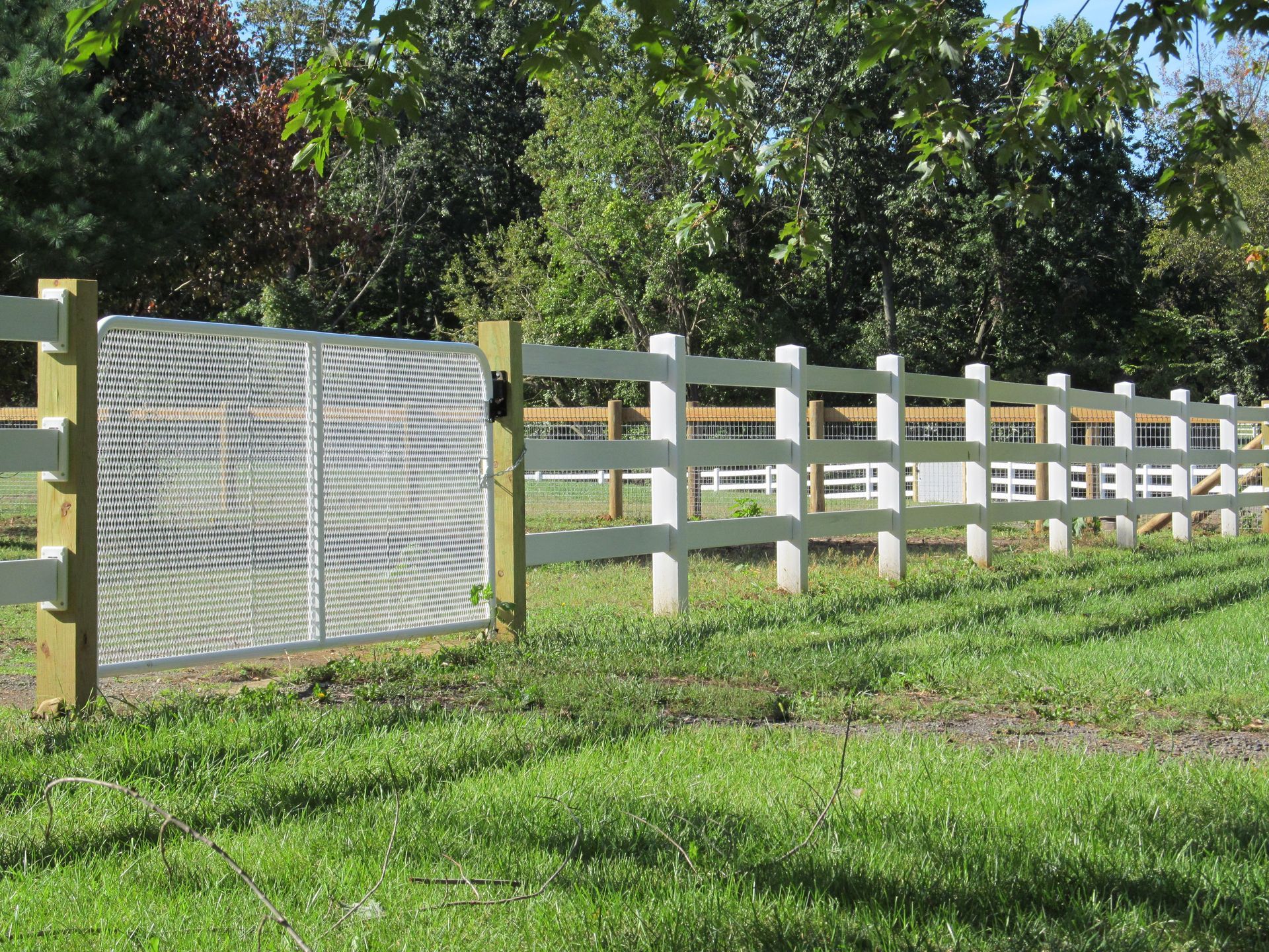 A wooden fence with a metal gate in the middle of a grassy field.