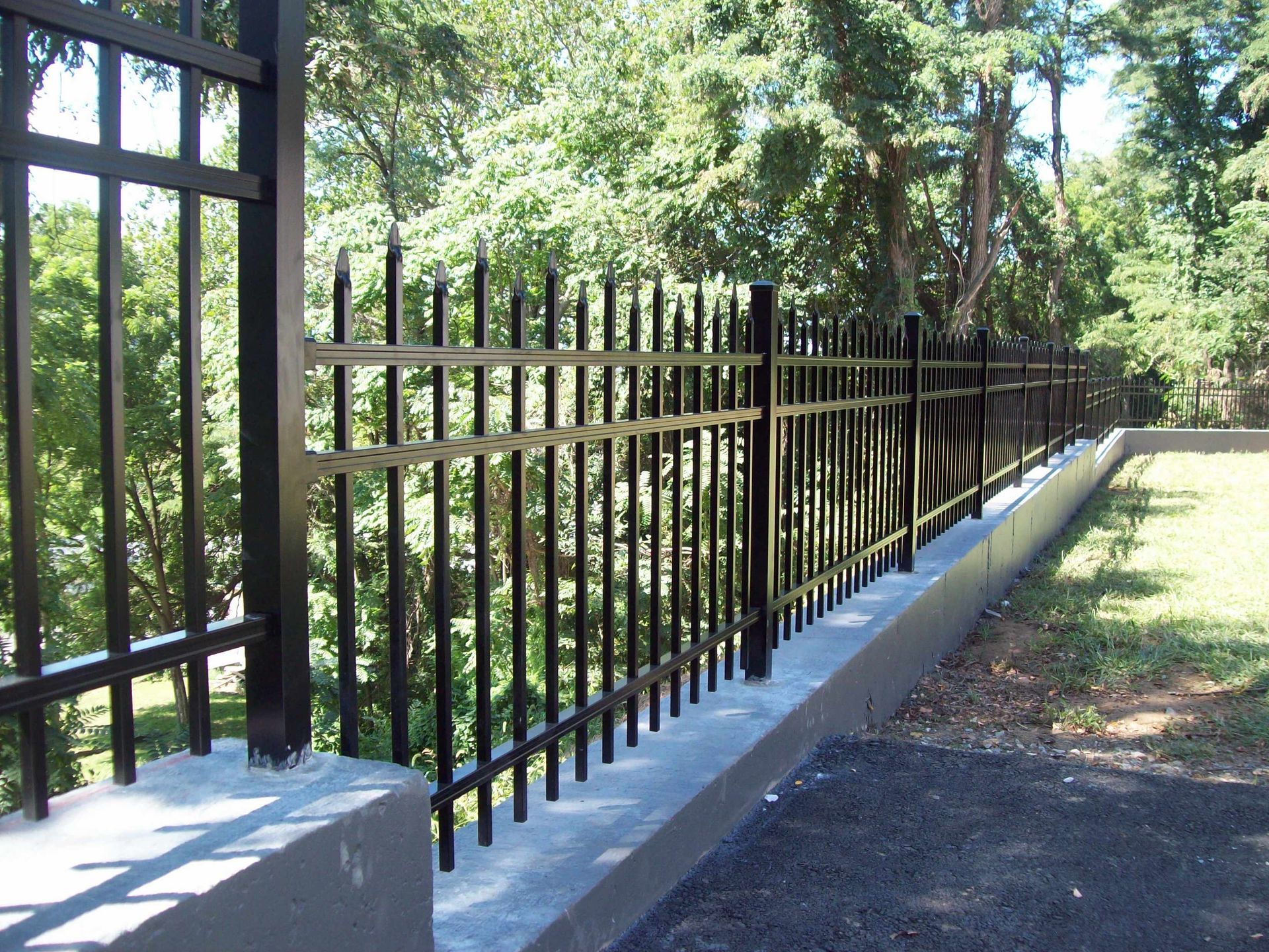 A black metal fence surrounds a concrete wall in a park