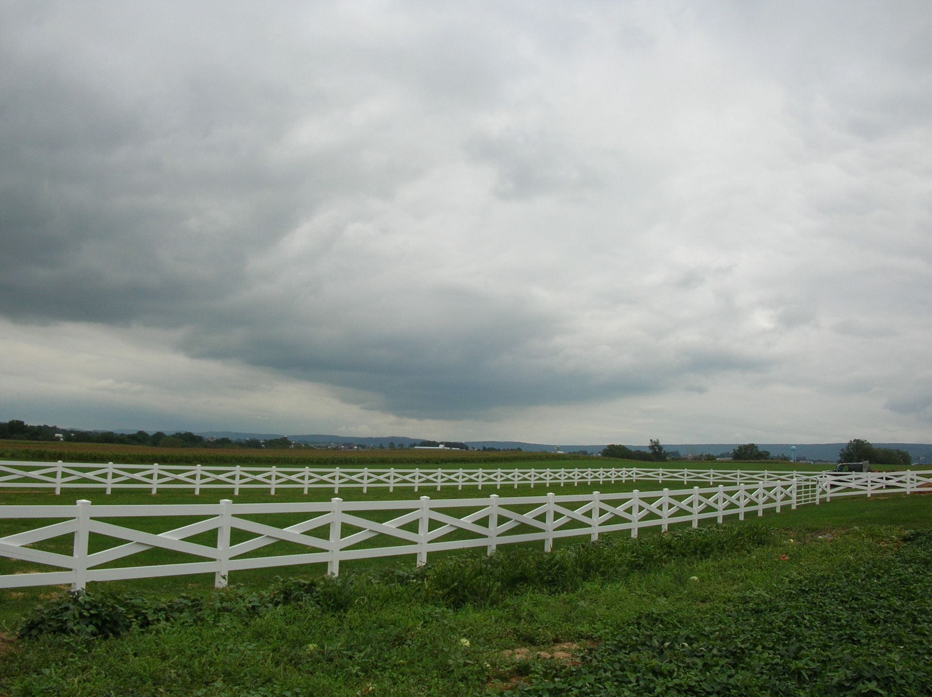 A white fence surrounds a grassy field on a cloudy day