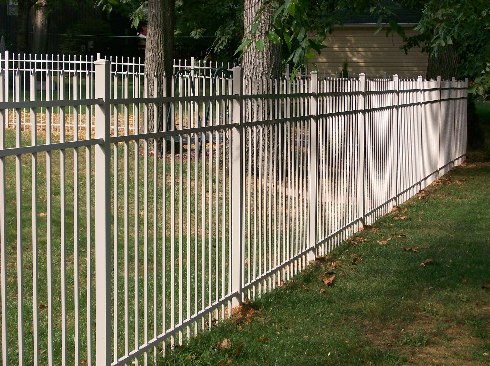 A white metal fence surrounds a lush green yard.