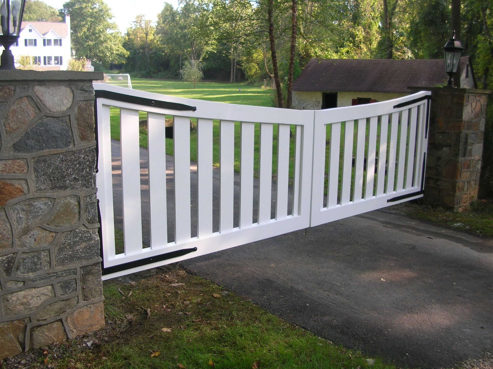 A white gate with black stripes is open to a driveway