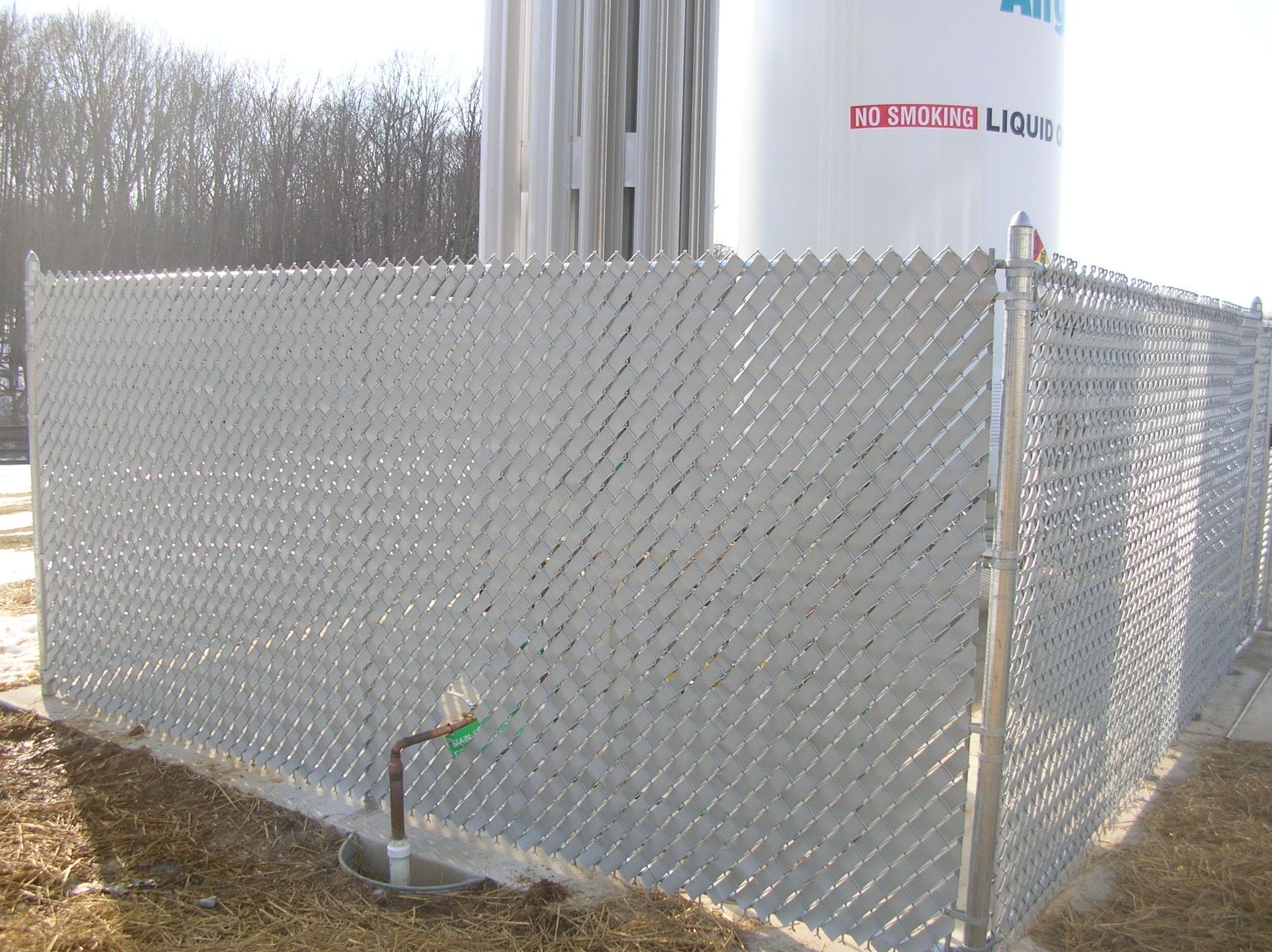 A chain link fence surrounds a large tank that says lg on it