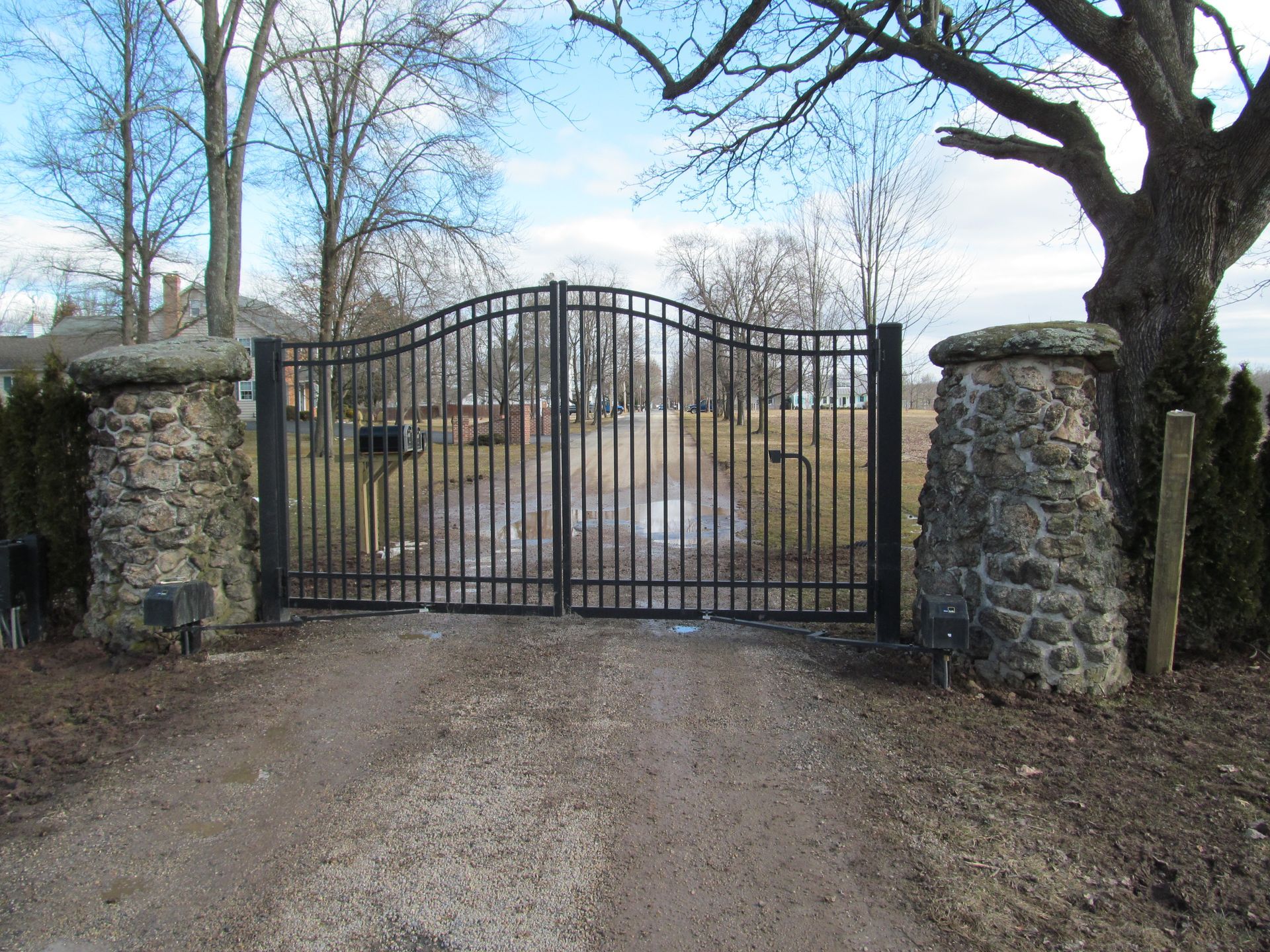 A metal gate is surrounded by stone pillars on the side of a dirt road.