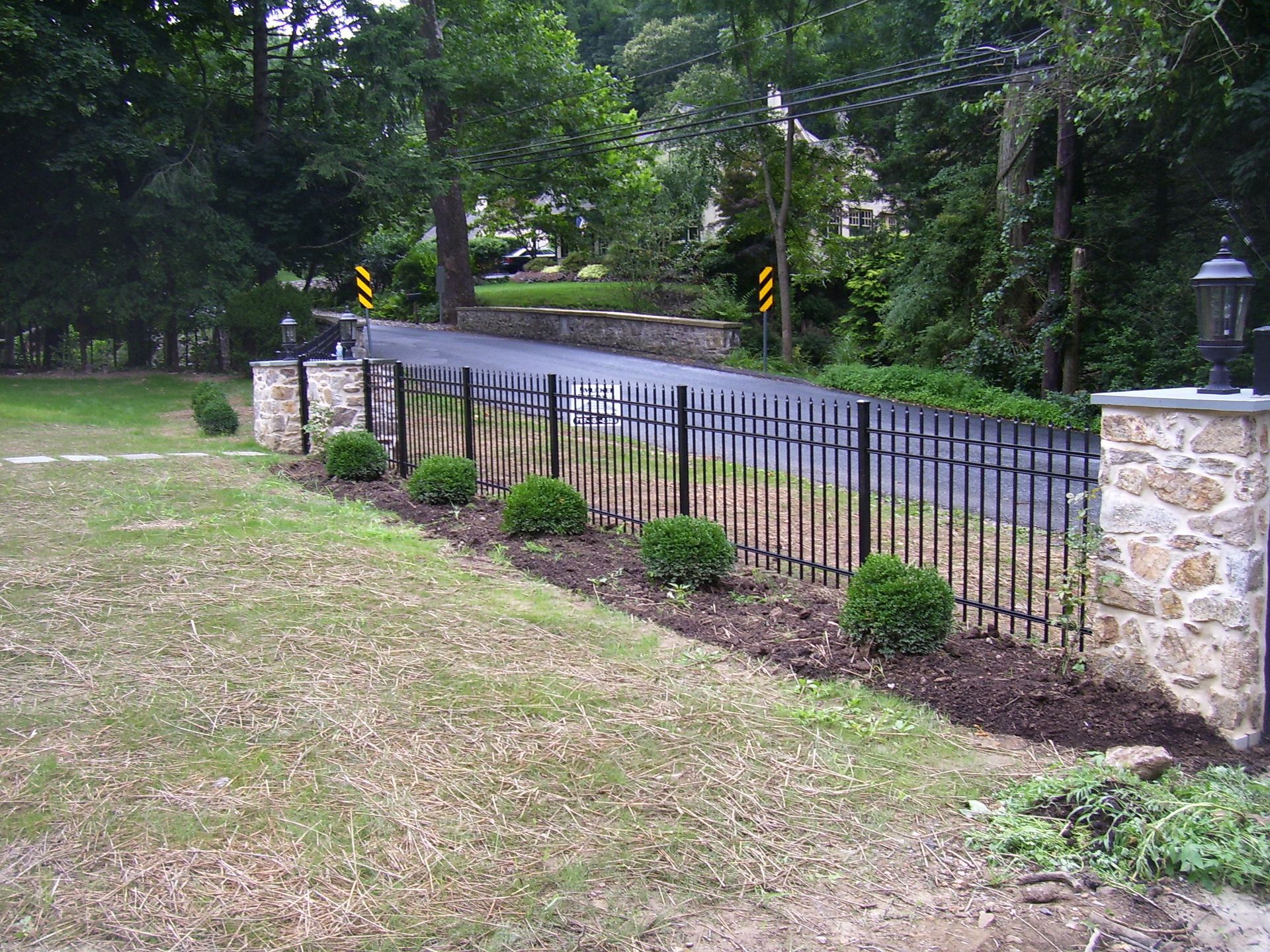 A black fence surrounds a grassy area next to a road.