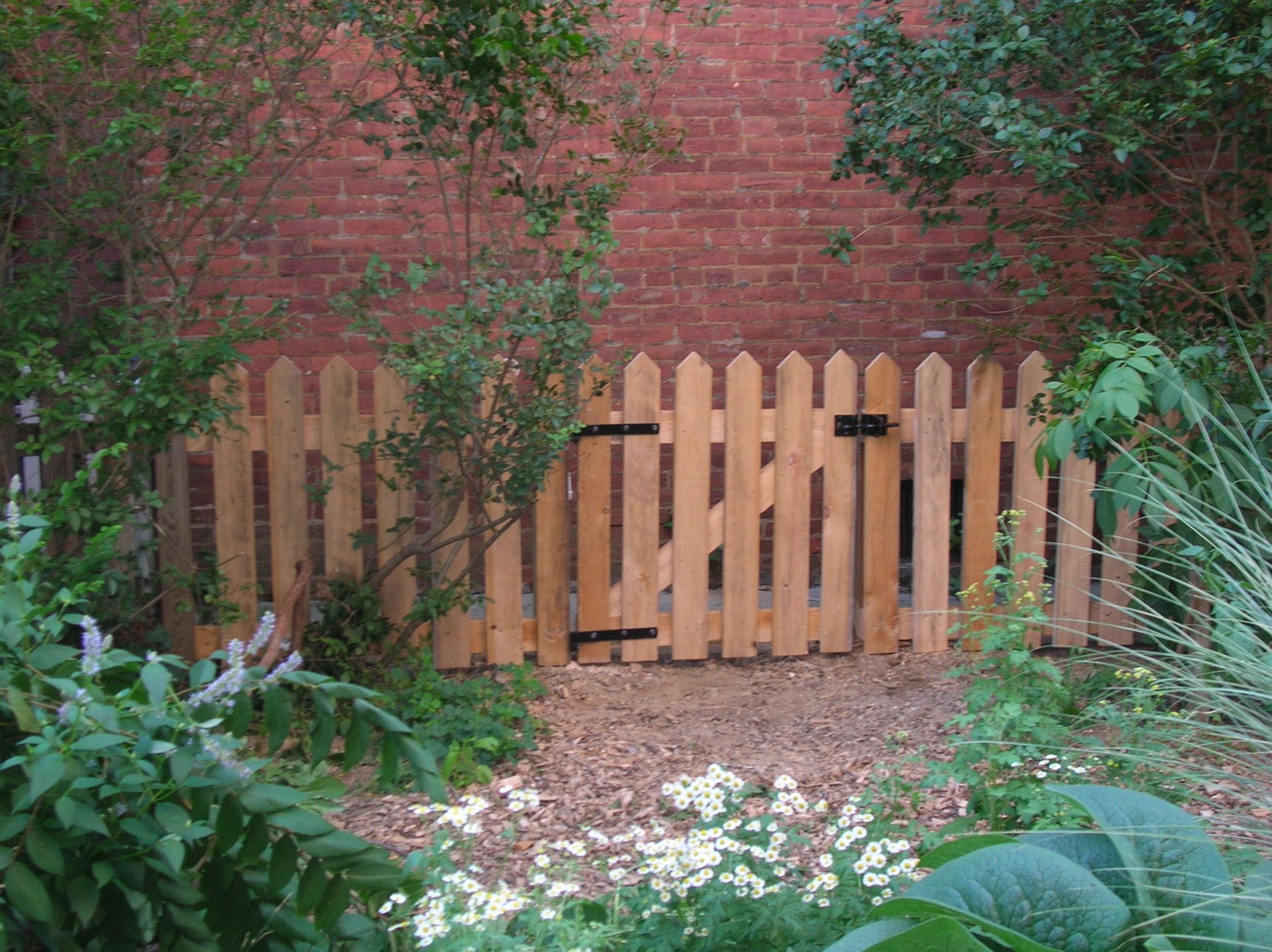 A wooden picket fence with a gate in front of a brick wall