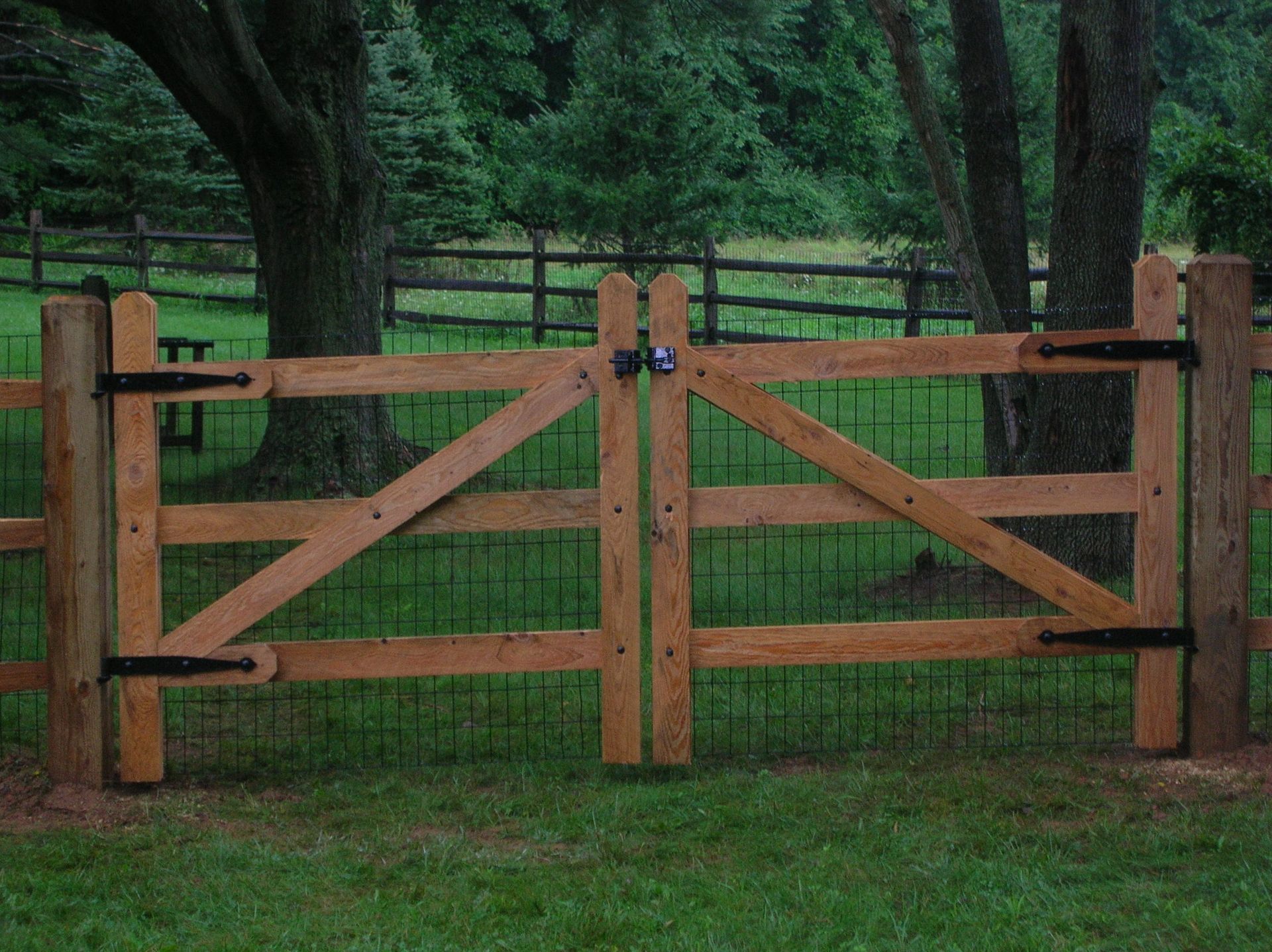 A wooden fence surrounds a grassy field with trees in the background