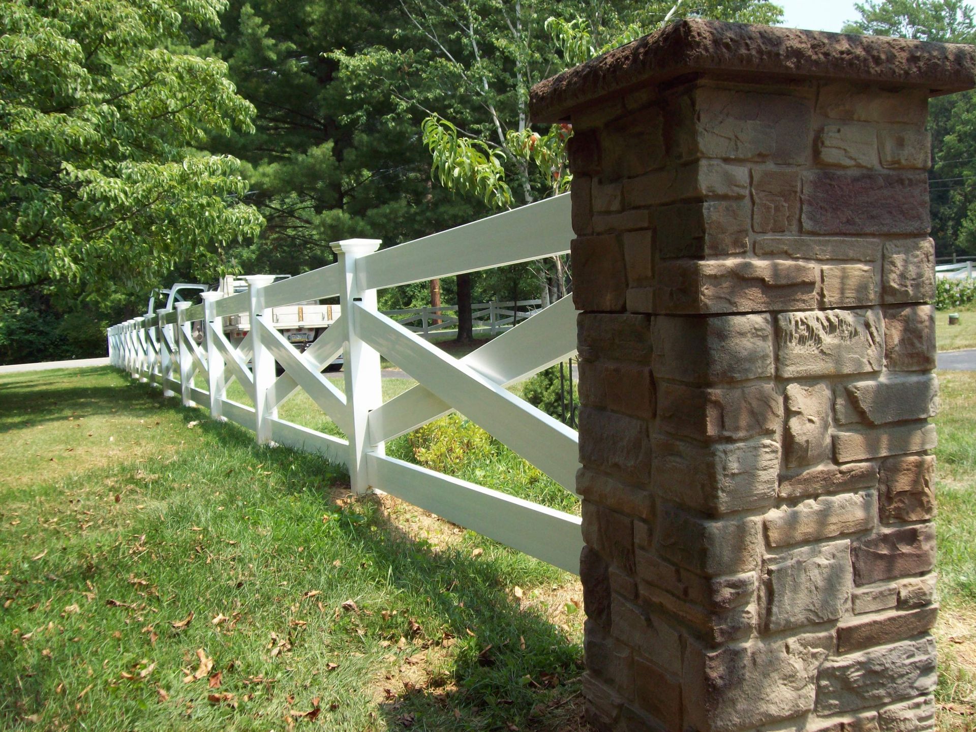 A white fence is next to a stone pillar