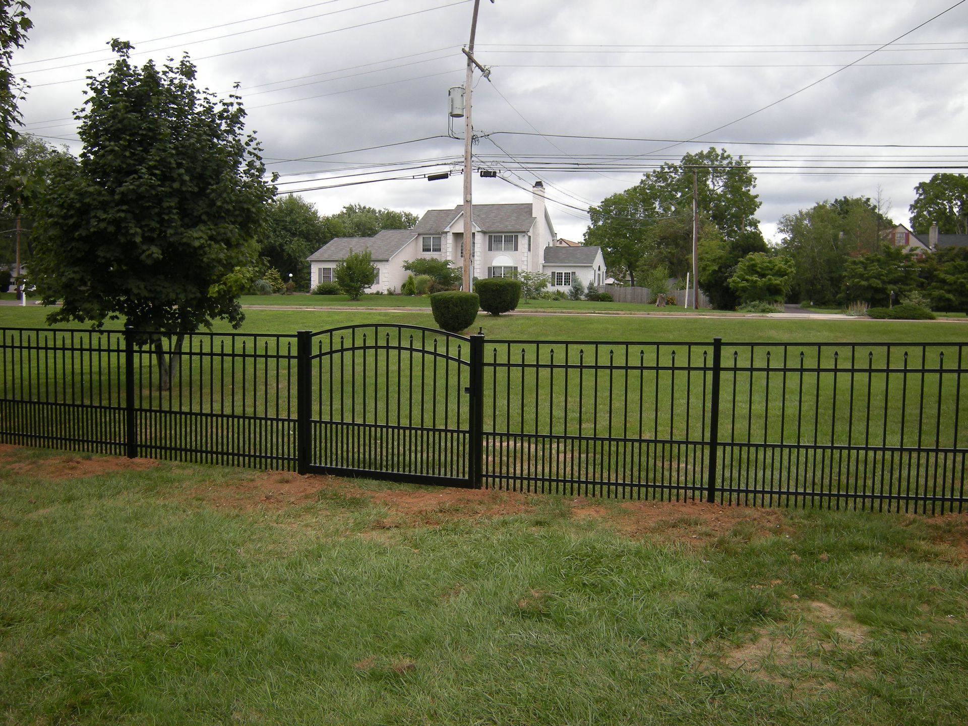 A black fence surrounds a grassy field with a house in the background