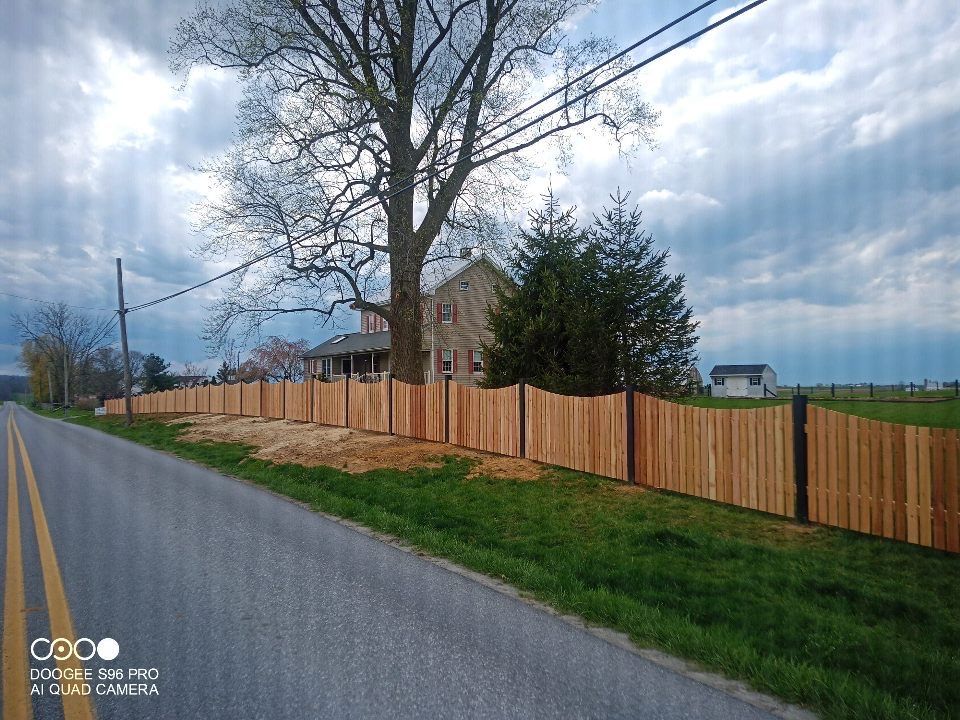 A wooden fence is along the side of a road next to a house.