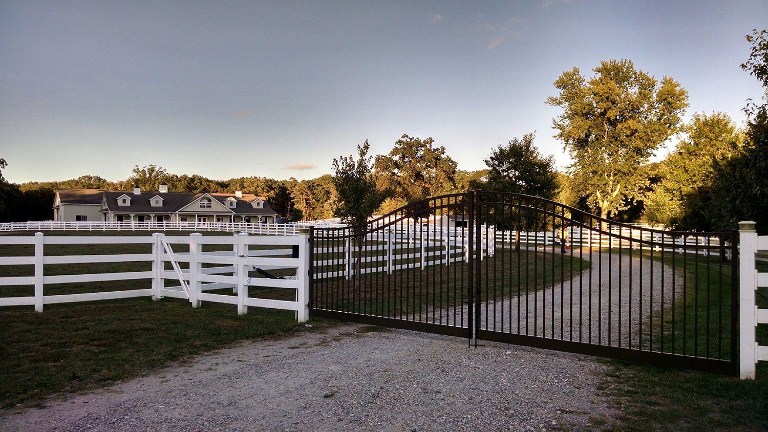 A white fence surrounds a gravel driveway leading to a house.