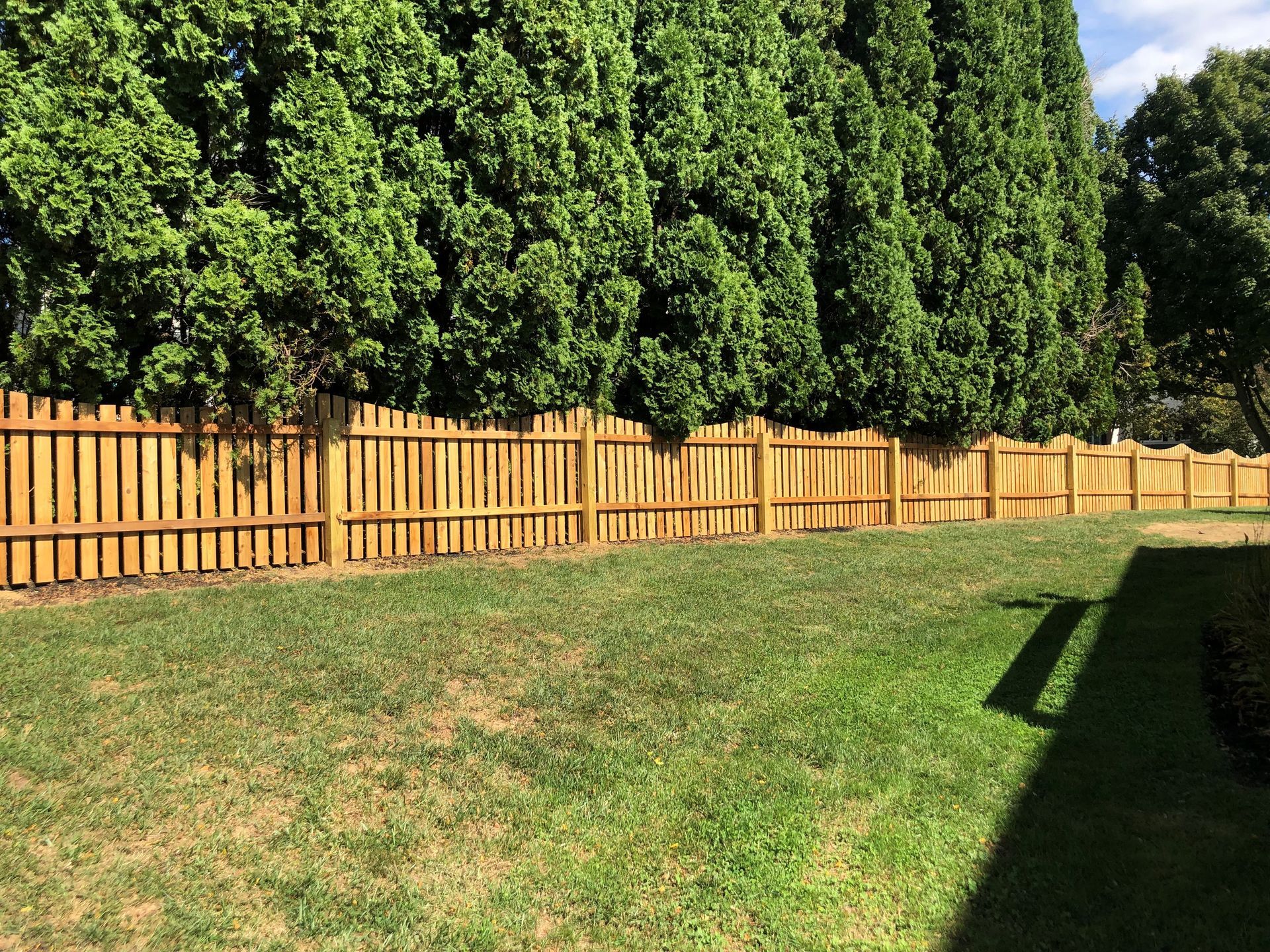 A long wooden fence surrounds a lush green yard.