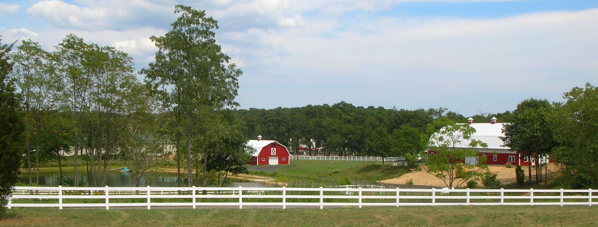 A white fence surrounds a farm with a red barn in the background