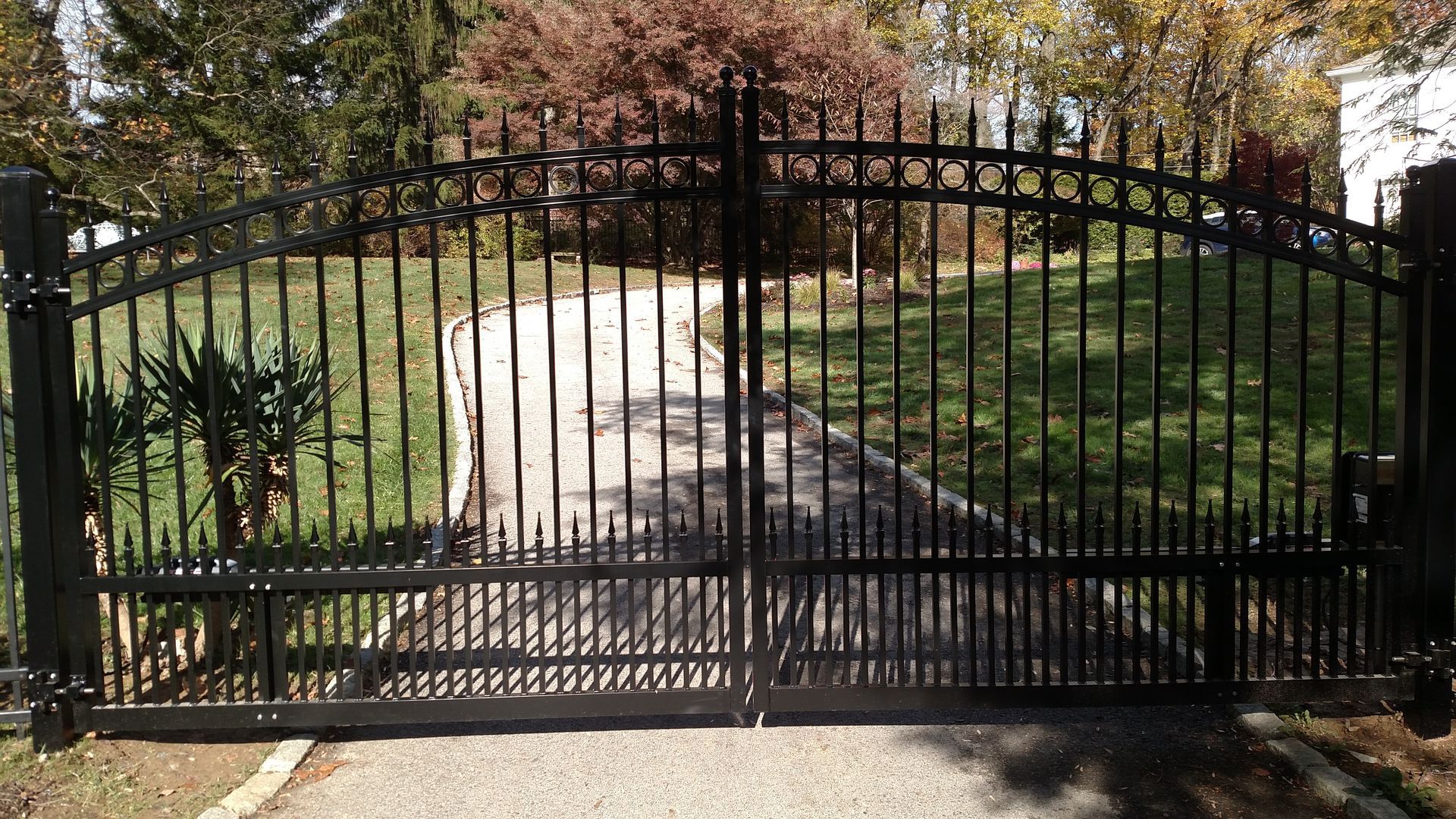 A black wrought iron gate is open to a driveway