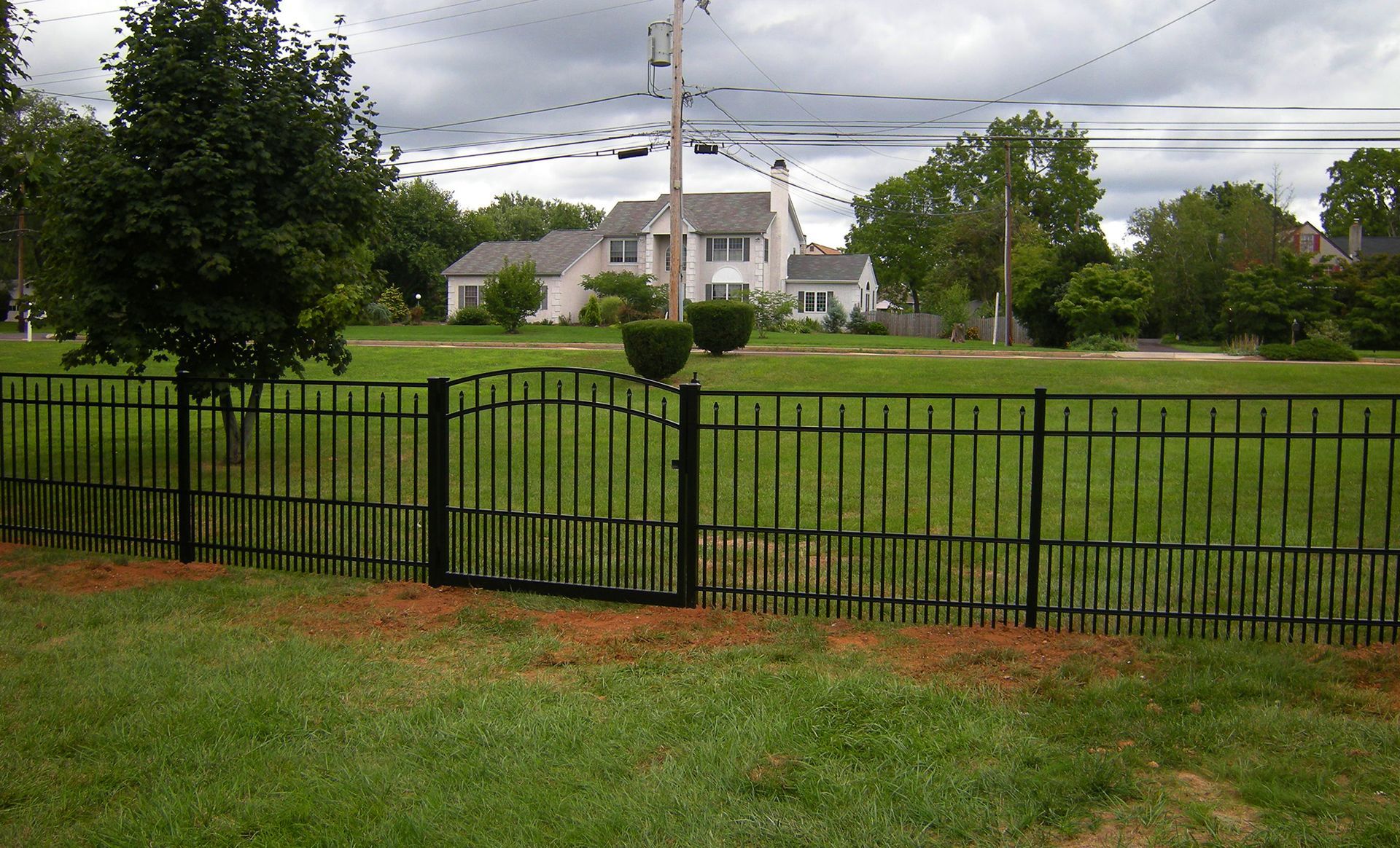 A black fence surrounds a grassy field with a house in the background