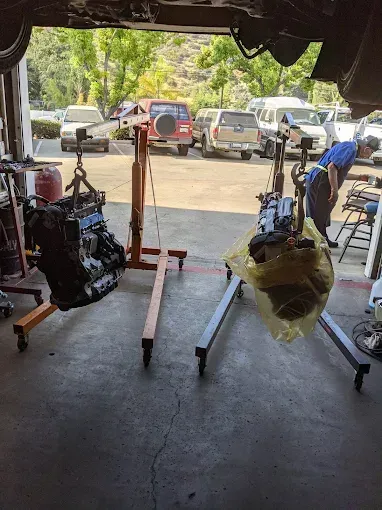 Two car engines suspended on stands inside a garage, mechanic working nearby.