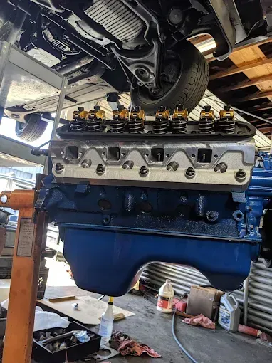 Blue engine block suspended by a lift. Cylinder head with gold springs is visible.