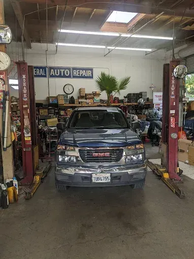 GMC truck in an auto repair shop bay, between two lifts. The shop has tools and parts.