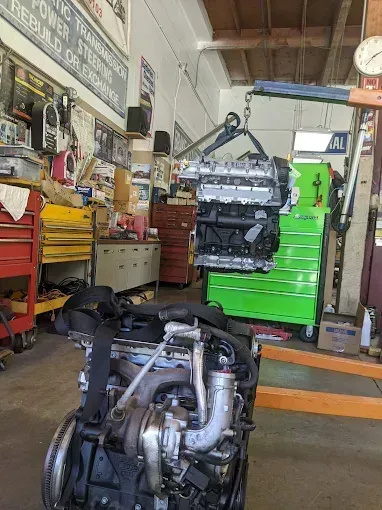 Engine hoisted above another engine in an auto repair shop. A green toolbox is in the background.