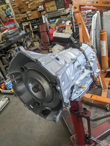 Silver transmission on a red stand in a cluttered garage, likely for repair.