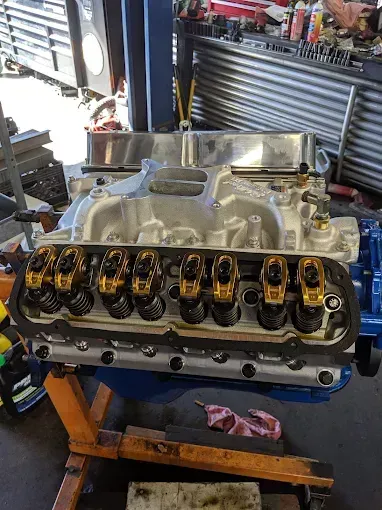 Blue engine block with gold rocker arms and silver intake manifold, likely in a shop.