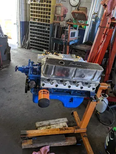 Blue engine on a stand in a garage, shiny chrome valve covers, orange filter.